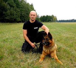 na trawie siedzi policjant przewodnik z psem służbowym